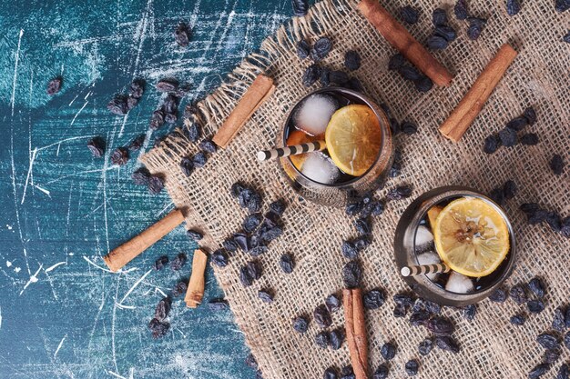 Sultana, cannelles citronnées avec une tasse de boisson sur bleu.