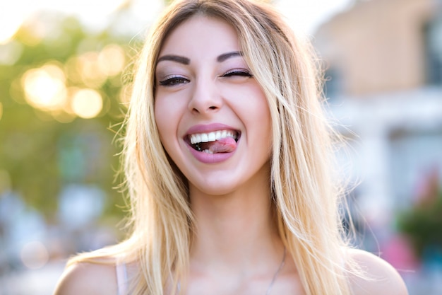 Photo gratuite sunny close up portrait of pretty blonde woman clignotant et montrant la langue, humeur positive ludique, couleurs pastel ensoleillées.