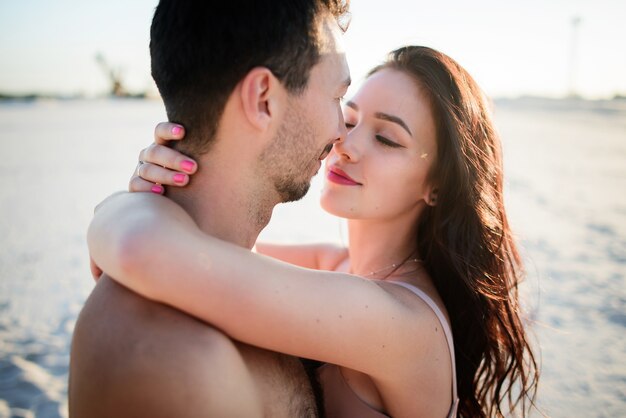 Une superbe brune embrasse son homme sur du sable blanc