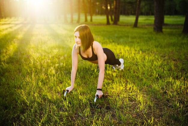 Superbe brunette se réchauffant et faisant des push ups sur la nature