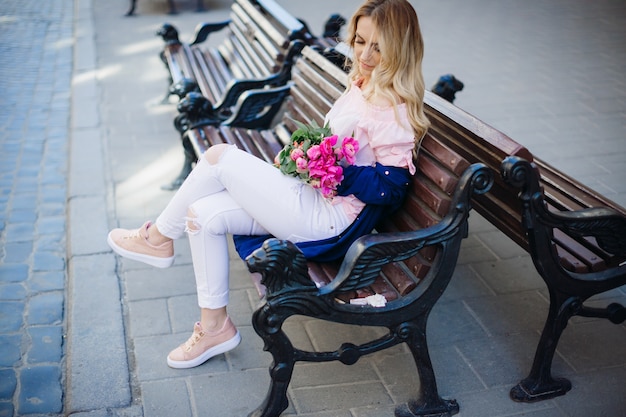 Photo gratuite superbe femme assise avec bouquet de pivoines sur le banc