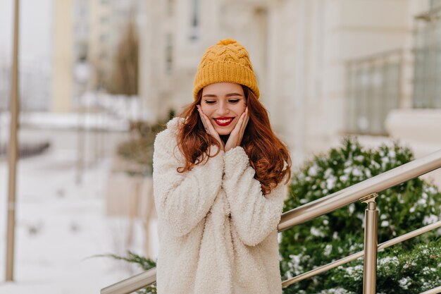 Superbe femme au gingembre posant avec un sourire sincère en journée d'hiver. Fille caucasienne positive s'amusant en décembre.