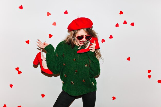 Superbe femme en béret rouge debout dans une pose confiante et tenant ses chaussures