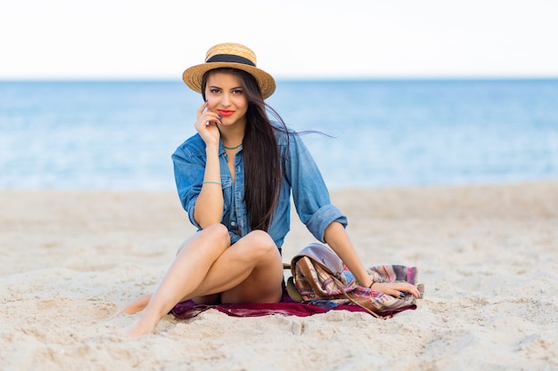 Superbe femme avec un corps bronzé, des lèvres rouges pleines et de longues jambes l posant sur la plage tropicale ensoleillée. Porter un haut court, un short et un chapeau de paille.