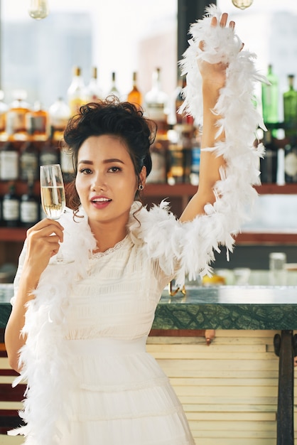 Superbe femme en déguisement et boa debout avec une flûte de champagne dans le bar