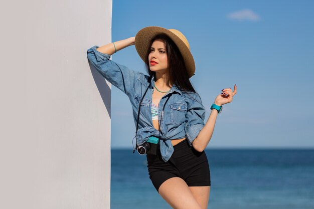 Superbe femme avec figure en short et chapeau de paille posant sur la plage.