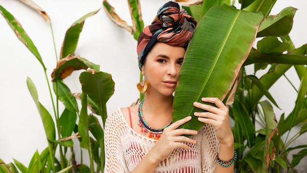 Photo gratuite superbe femme avec turban sur la tête, boucles d'oreilles colorées et collier boho posant