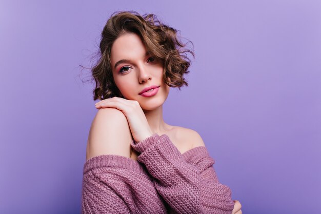 Superbe fille européenne aux lèvres roses posant rêveur Photo intérieure d'une femme brune raffinée aux cheveux courts isolée sur un mur violet.