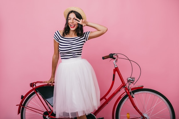 Photo gratuite superbe fille latine en jupe luxuriante debout près de vélo rouge. adorable femme dans des vêtements à la mode posant avec plaisir.