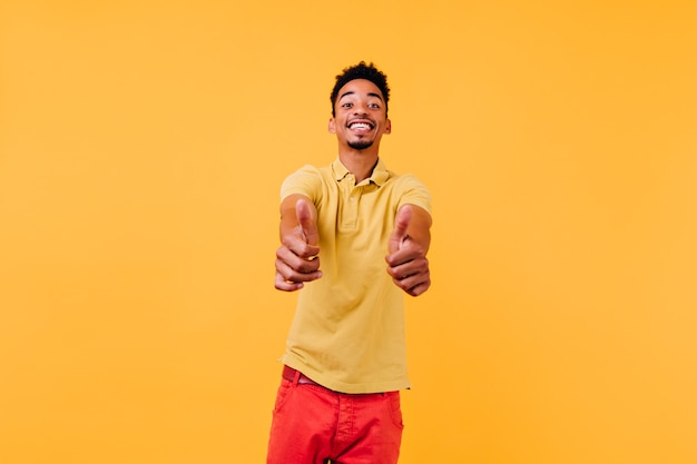 Superbe homme aux cheveux courts exprimant des émotions sincères. Gars inspiré en t-shirt jaune montrant les pouces vers le haut.