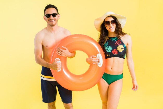 Superbe jeune femme en bikini et bel homme charmant partageant un gonflable de sauveteur et sur le point d'entrer dans la piscine pendant une chaude journée