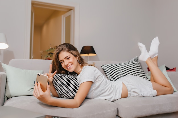 Superbe jeune femme en chaussettes blanches allongée sur le canapé et faisant selfie