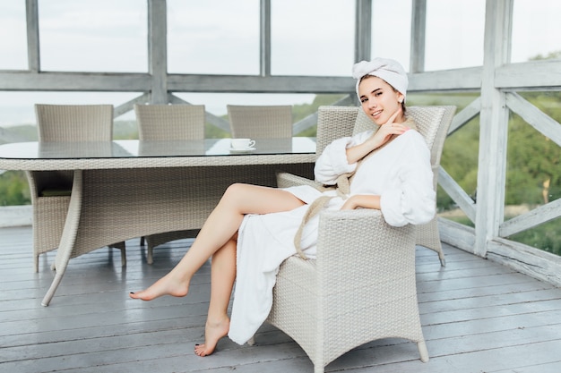 Superbe jeune femme en robe blanche, assise sur la terrasse d'été chez elle. Notion du matin.