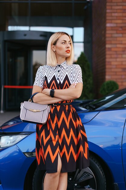 Superbe jeune femme waring dress posant devant sa voiture à l'extérieur, conducteur de propriété