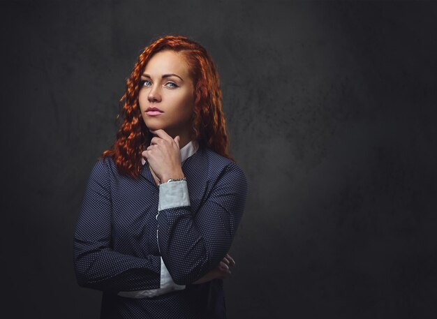 Superviseure rousse vêtue d'un costume élégant sur fond gris.