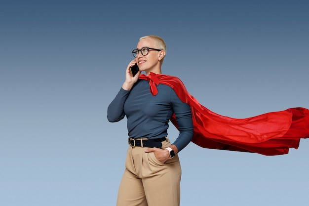 Photo gratuite superwoman avec cape parlant sur smartphone