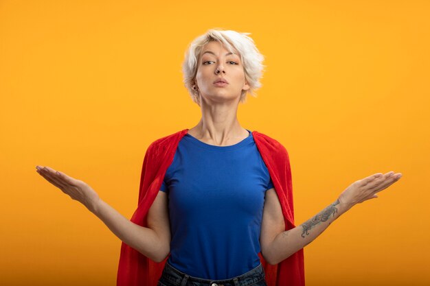 Superwoman confiant avec cape rouge tient les mains ouvertes isolé sur mur orange