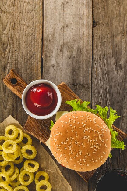 Surface en bois avec hamburger appétissant, anneaux d&#39;oignons et sauce tomate