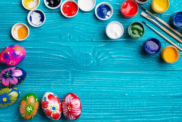 surface en bois avec des oeufs de Pâques et des pots de peinture de couleur