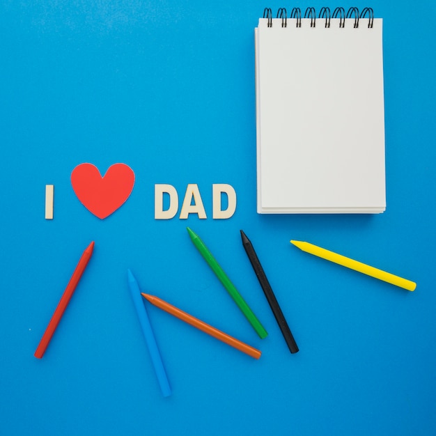 La surface du jour du père avec des crayons de couleur et un cahier vierge