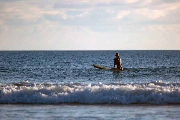 Surfer assis dans l'océan au coucher du soleil