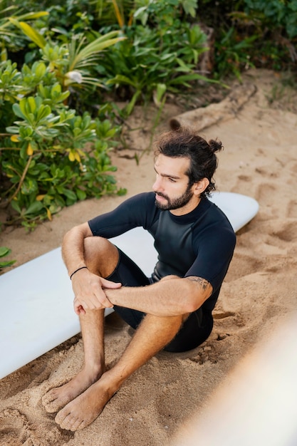 Photo gratuite surfer et sa planche de surf assis sur le sable