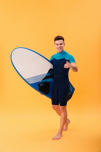 Surfeur souriant marchant avec planche de surf et pointant