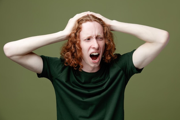 Surpris attrapé la tête jeune beau mec portant un t-shirt vert isolé sur fond vert