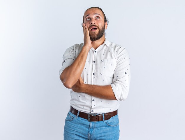 Surpris bel homme adulte portant des lunettes en gardant la main sur le visage en levant isolé sur mur blanc avec espace de copie