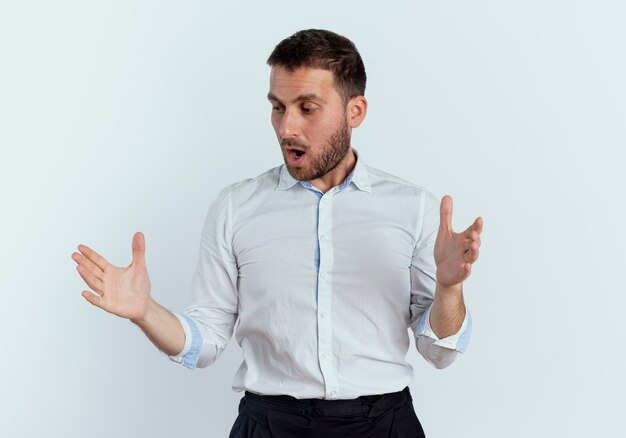 Surpris bel homme fait semblant de tenir quelque chose et regarde la main isolé sur un mur blanc