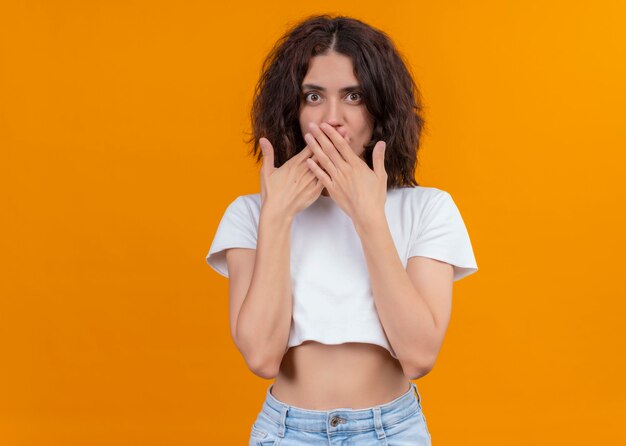 Surpris belle jeune femme mettant les mains sur la bouche sur un mur orange isolé avec espace copie