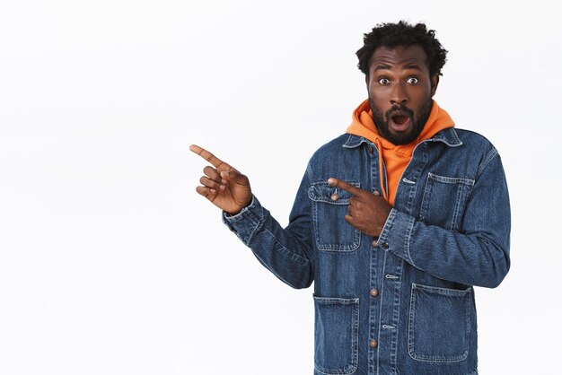 Surpris, excité beau afro-américain barbu en veste en jean, sweat à capuche orange d'automne, haletant étonné, bouche bée sans voix