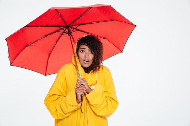 Surpris femme africaine en imperméable posant avec parapluie