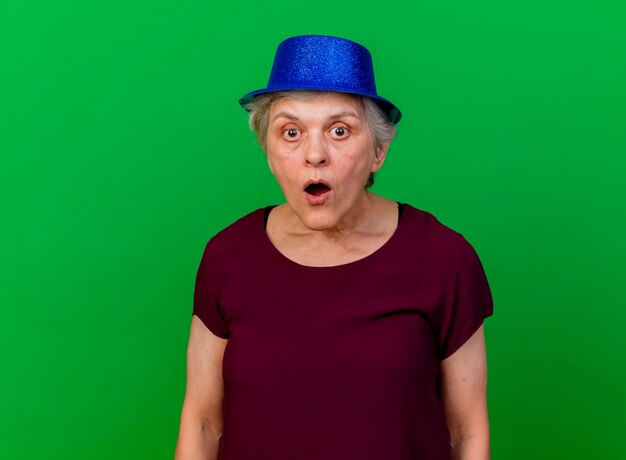 Surpris femme âgée portant chapeau de fête regarde la caméra sur le vert