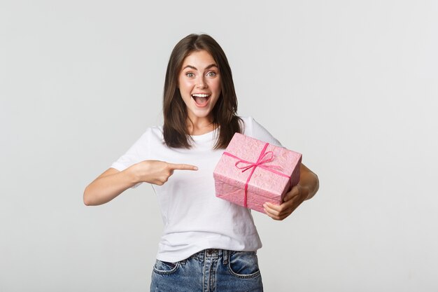 Surpris heureuse jeune femme souriante et pointant le doigt au cadeau emballé.