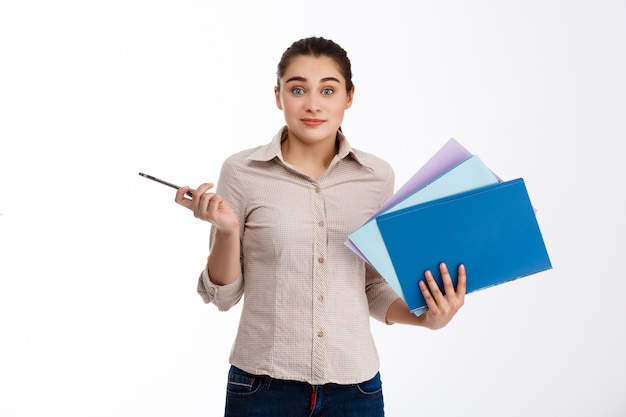 Surpris jeune belle femme d'affaires détenant des dossiers colorés sur mur blanc