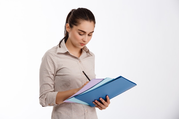 Surpris jeune belle femme d'affaires écrit sur des dossiers colorés sur mur blanc