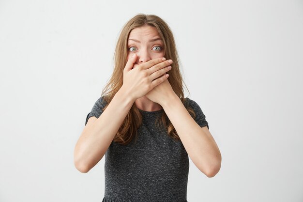 Surpris jeune belle fille fermant la bouche derrière les mains.