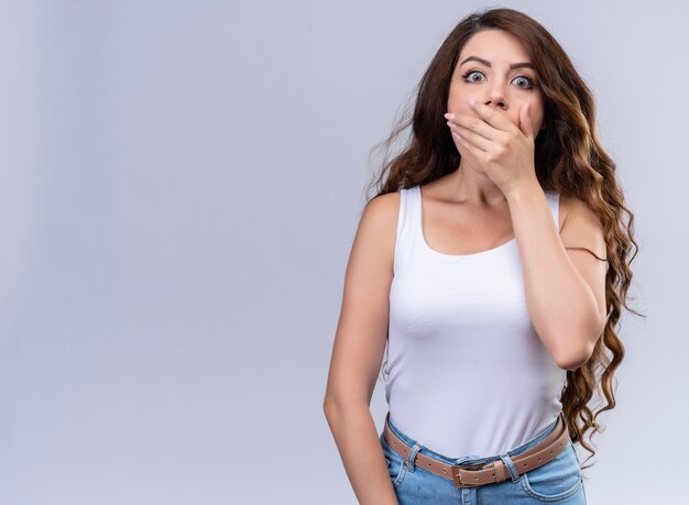 Surpris jeune belle fille fermant la bouche avec la main sur un mur blanc isolé avec copie espace