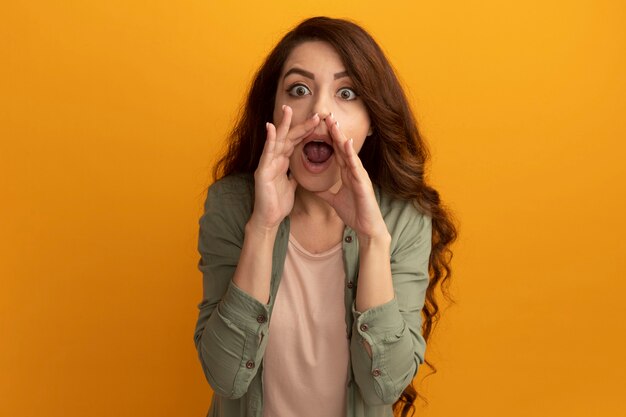 Surpris jeune belle fille portant un t-shirt vert olive appelant quelqu'un isolé sur mur jaune