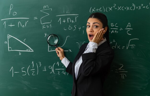 surpris jeune enseignante debout devant le tableau noir mettant la main sur la joue en classe