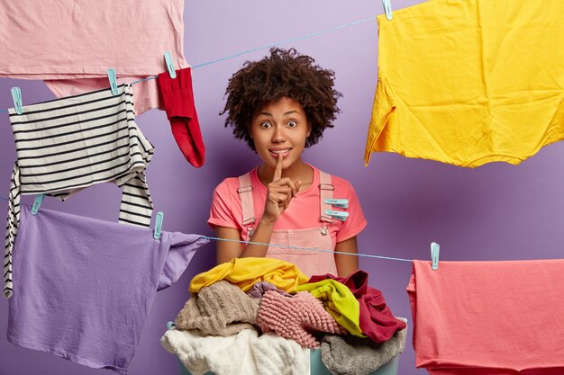 Surpris jeune femme avec un afro posant avec du linge en salopette