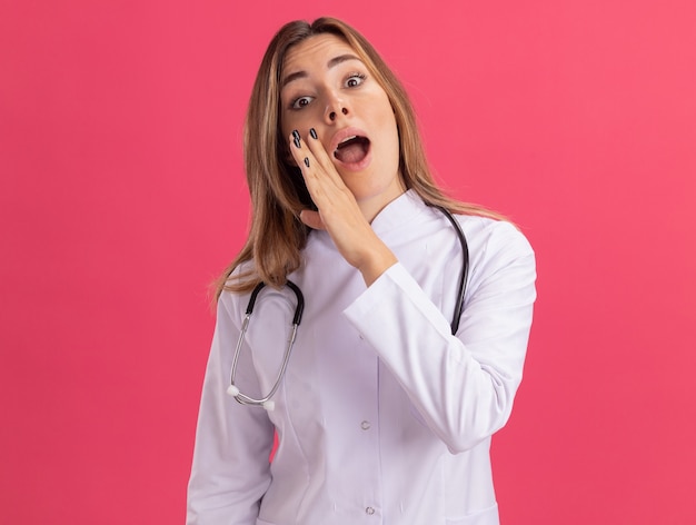 Surpris Jeune Femme Médecin Portant Une Robe Médicale Avec Chuchotements Stéthoscope Isolé Sur Mur Rose