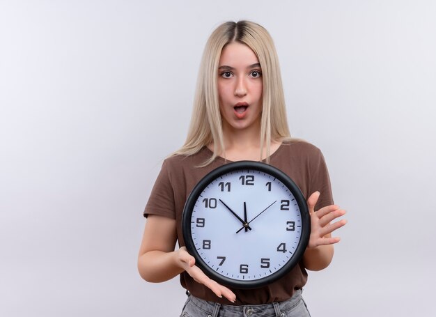 Surpris jeune fille blonde tenant horloge sur mur blanc isolé avec copie espace