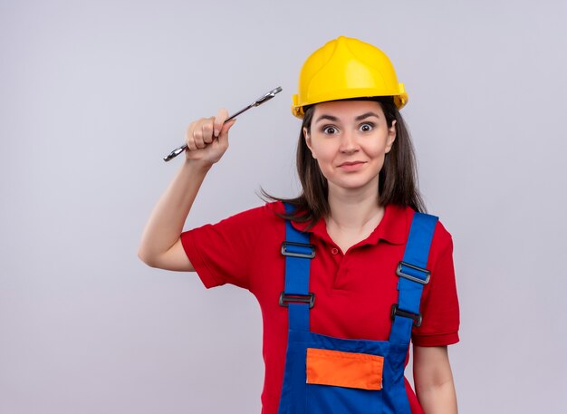 Surpris jeune fille constructeur détient la clé de l'atelier et regarde la caméra sur fond blanc isolé avec copie espace