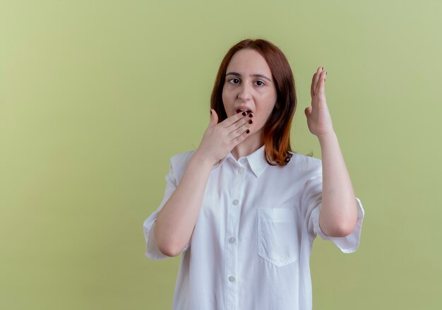 Photo gratuite surpris jeune fille rousse avec la bouche couverte de main et levant la main isolé sur vert olive