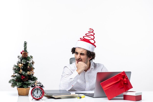 Surpris jeune homme d'affaires avec drôle de chapeau de père Noël parlant à quelqu'un au bureau sur fond blanc