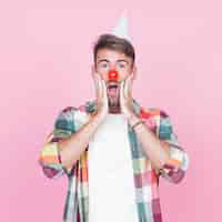 Photo gratuite surpris jeune homme avec nez de clown rouge debout sur fond rose