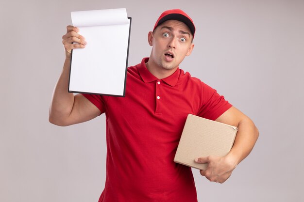 Surpris jeune livreur en uniforme avec capuchon tenant la boîte et soulever le presse-papiers isolé sur mur blanc