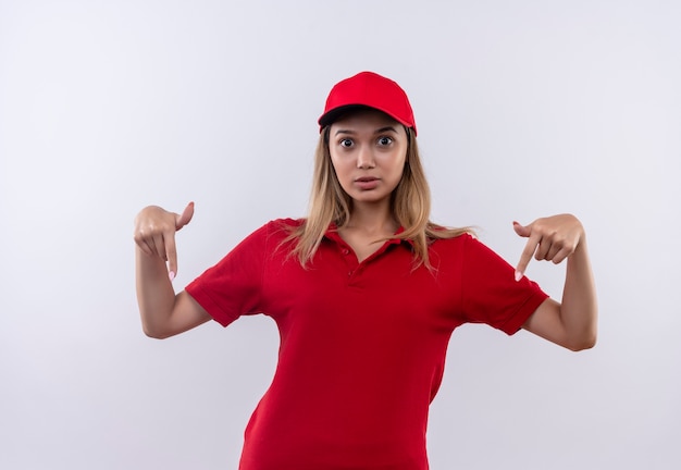 Surpris jeune livreuse portant l'uniforme rouge et pointe vers le bas isolé sur blanc